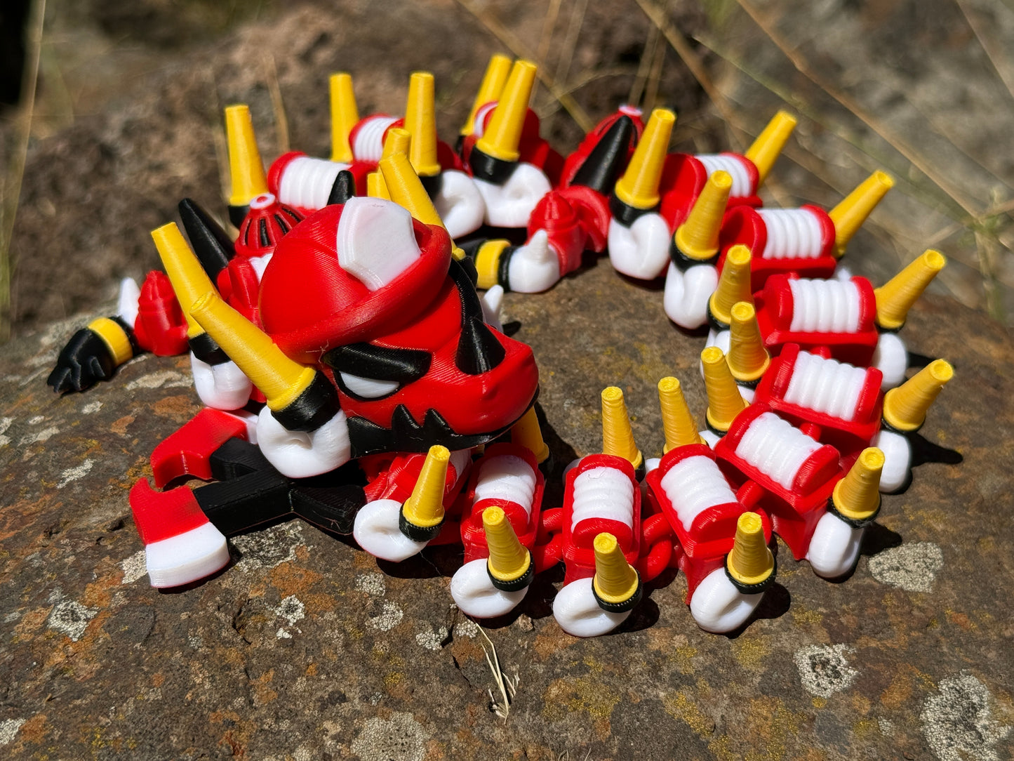 firefighter dragon 3d printer with red, white, and yellow segments on a rocky surface with a 2-axe tail