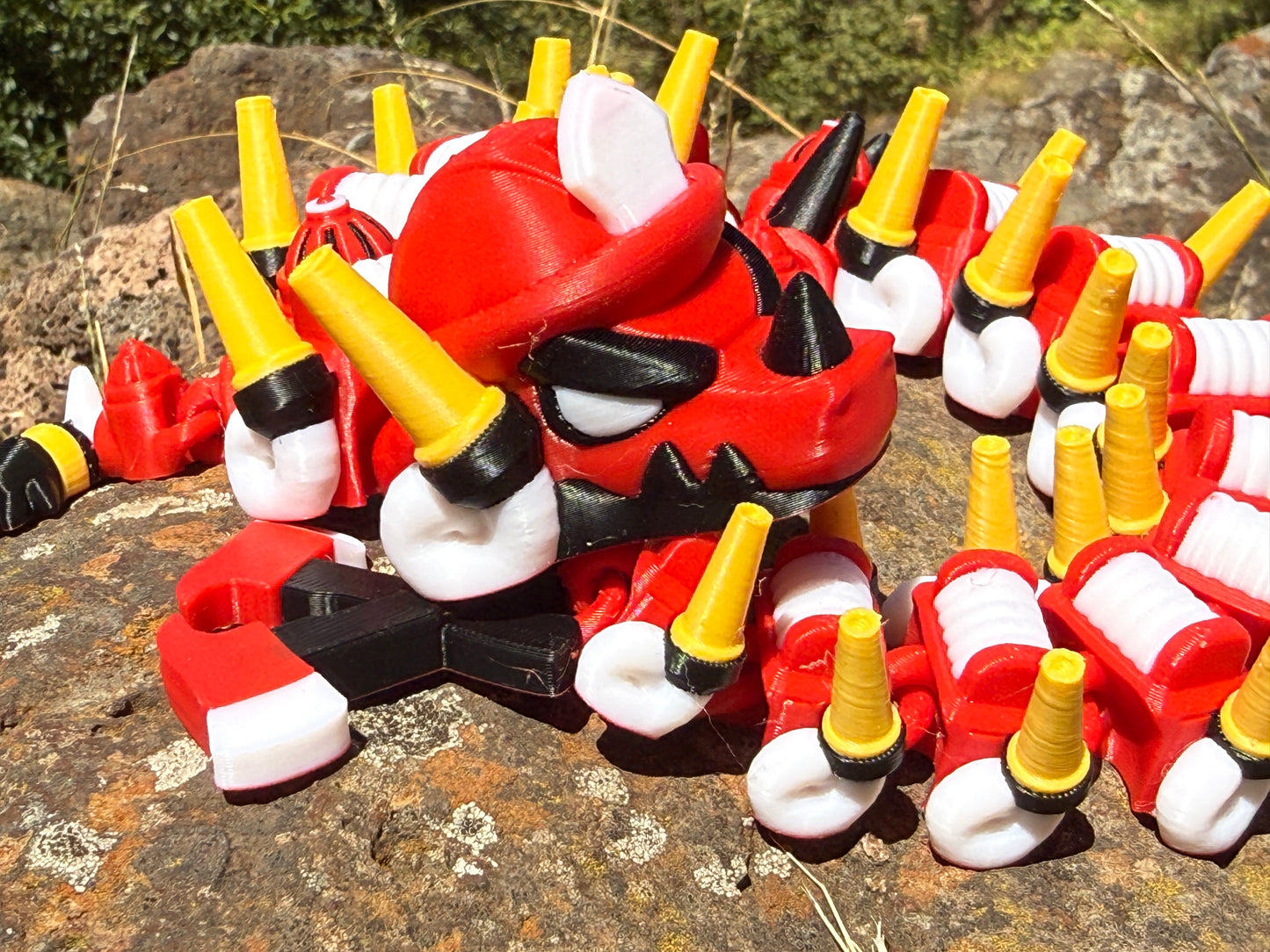 firefighter dragon 3d printer with red, white, and yellow segments on a rocky surface with a 2-axe tail