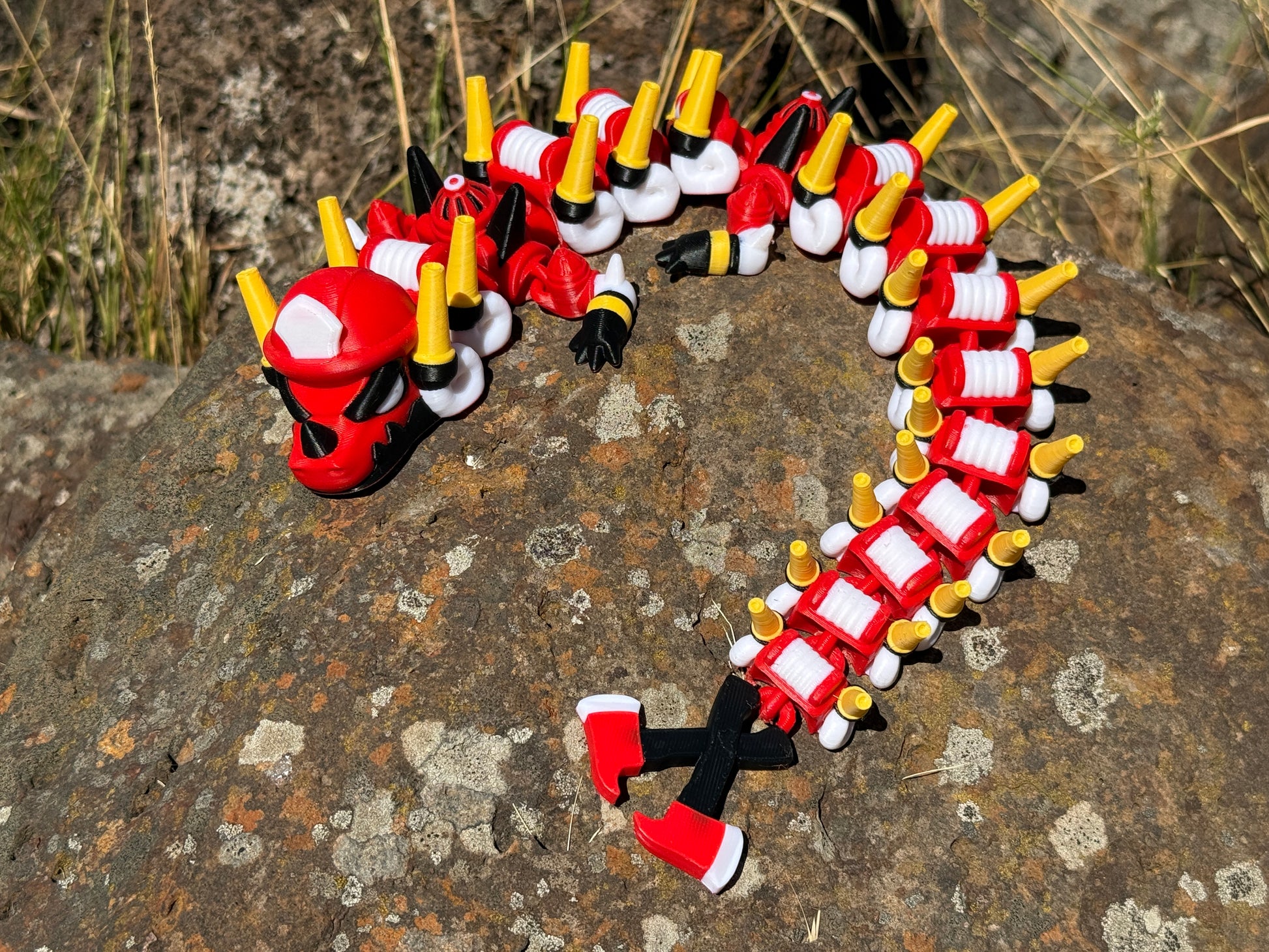 firefighter dragon 3d printer with red, white, and yellow segments on a rocky surface