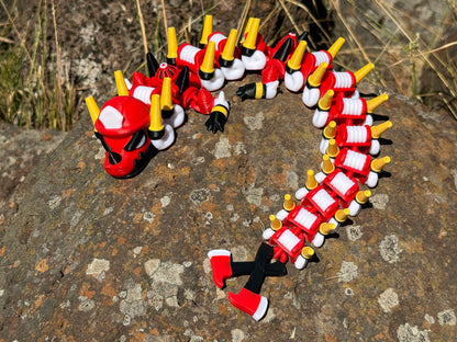 firefighter dragon 3d printer with red, white, and yellow segments on a rocky surface