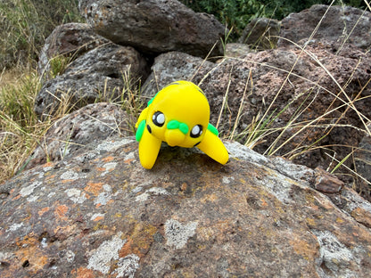 Yellow 3d printed budgie with green accents on a rock in a natural setting