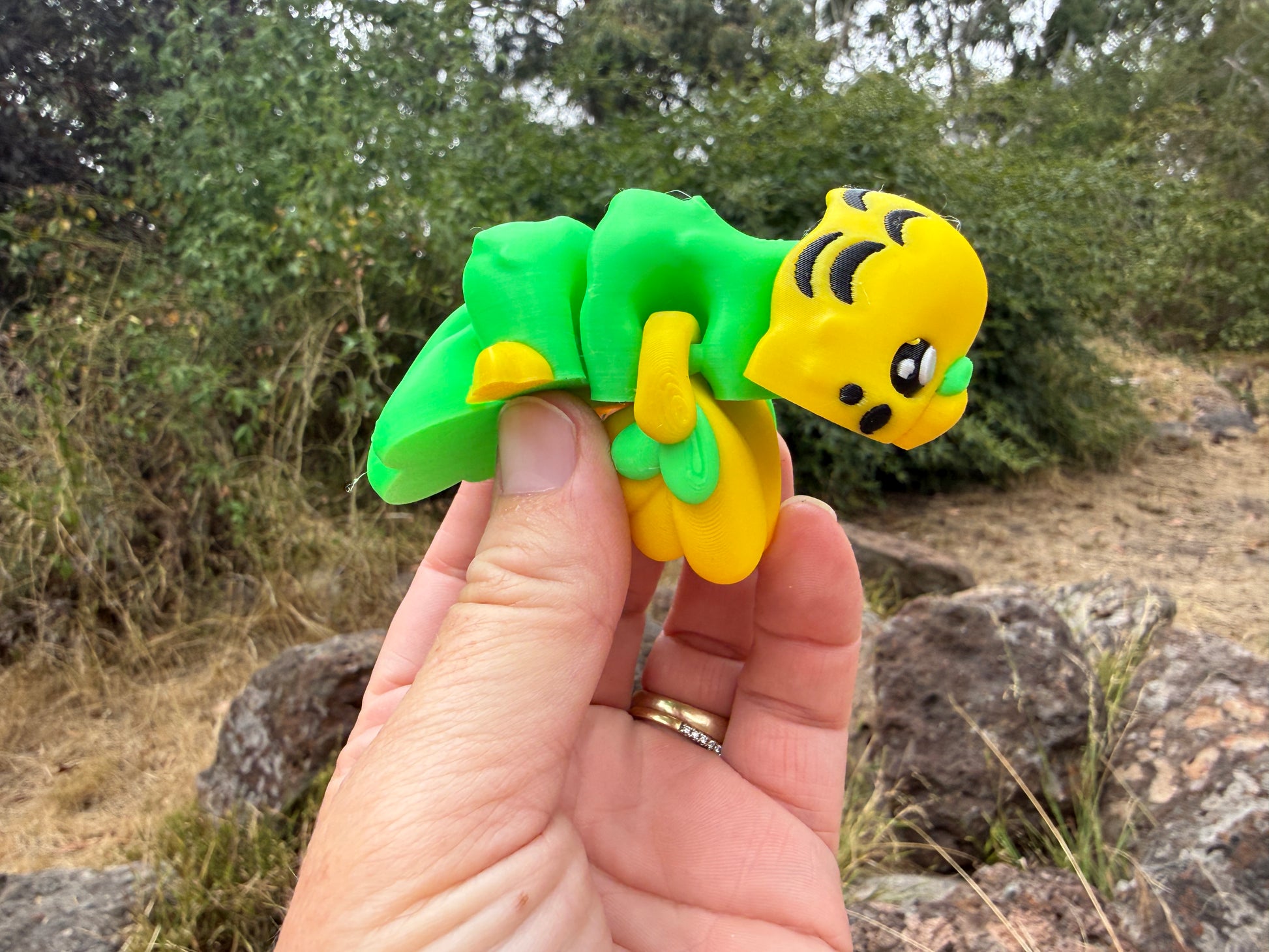 3d printed budgie yellow and green held by a hand with a natural background