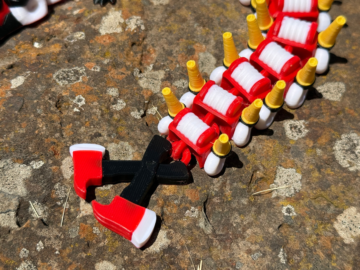 firefighter dragon 3d printer with red, white, and yellow segments on a rocky surface with a 2-axe tail