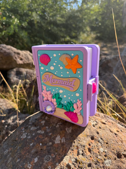 Colour purple, blue, white, green, pink 3d printed book with mermaid design on a rock