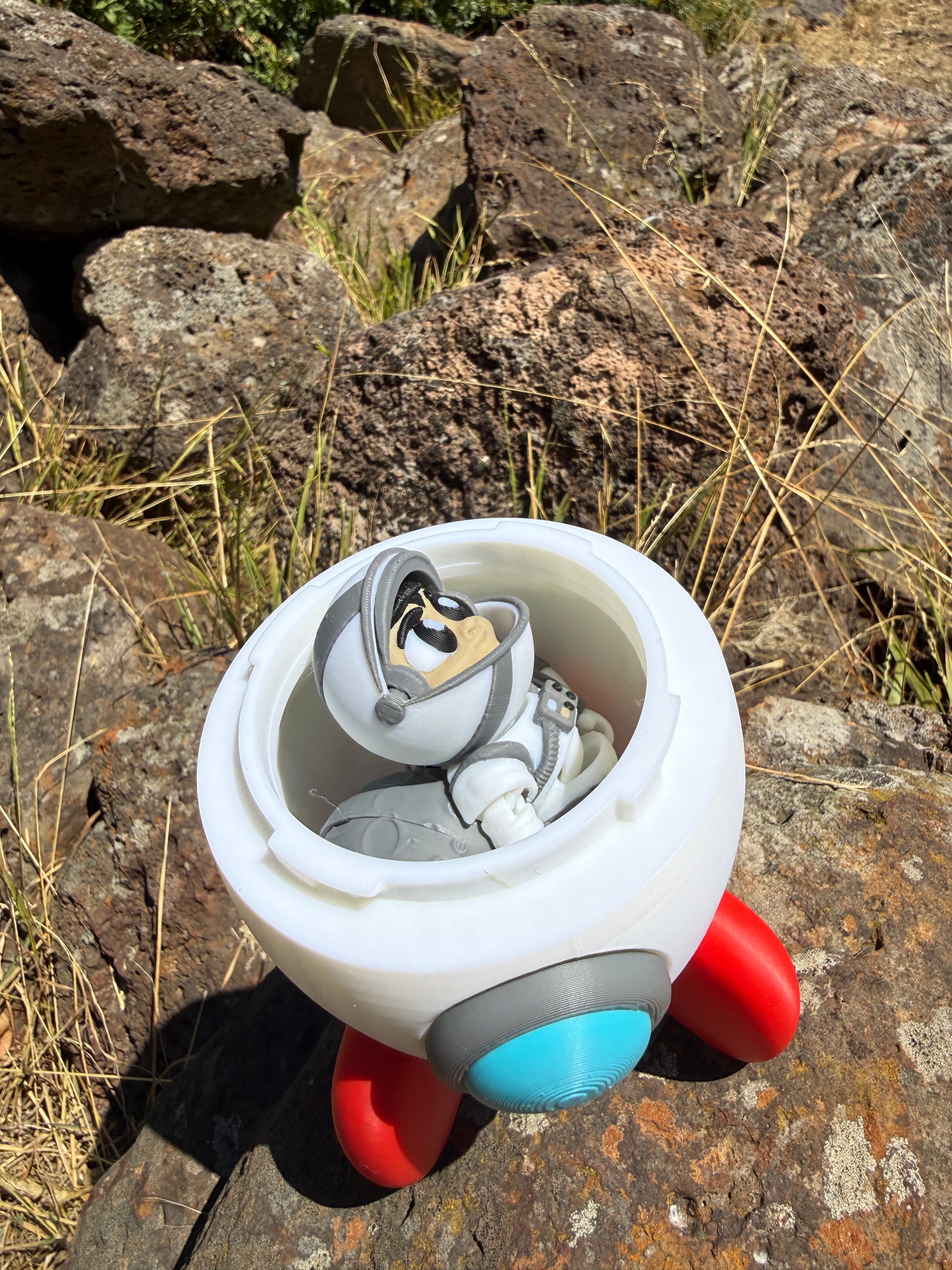 3d printed with astronauts inside half open rocket. rocket has blue and red and white on it