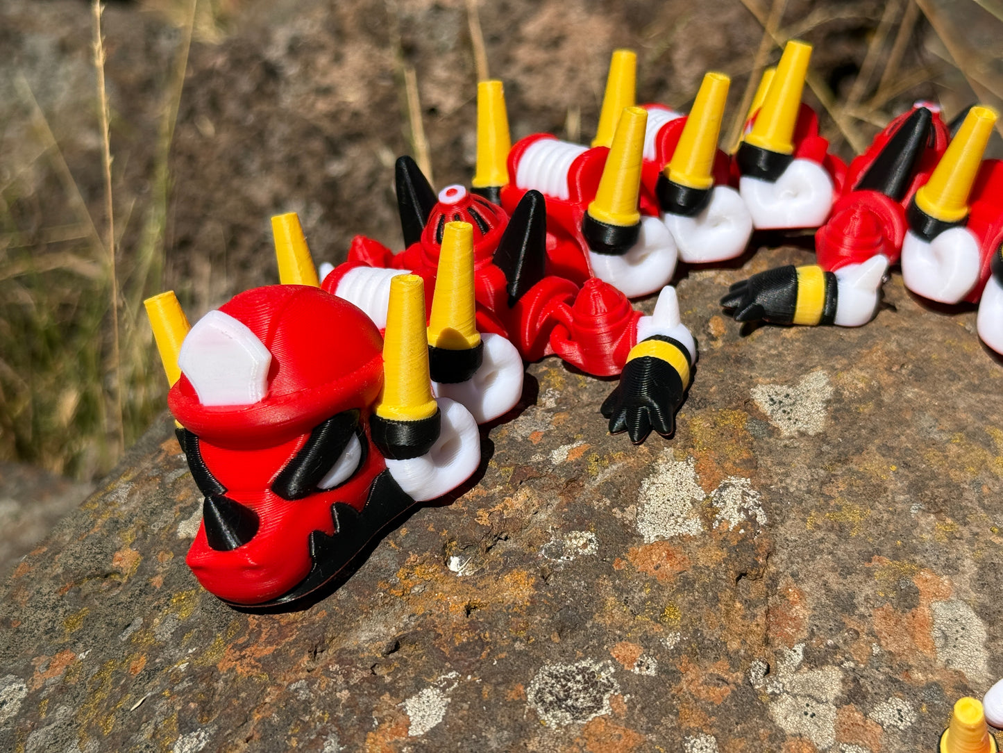 firefighter dragon 3d printer with red, white, and yellow segments on a rocky surface 