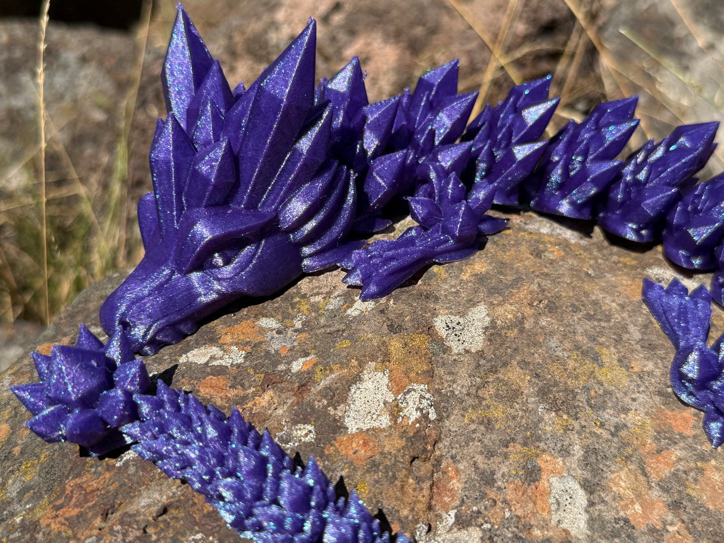 Purple sparkle 3d printed dragon
on a rocky surface