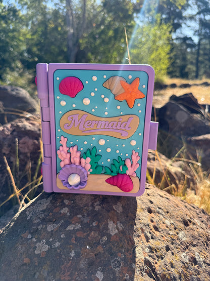 Colour purple, blue, white, green, pink 3d printed book with mermaid design on a rock