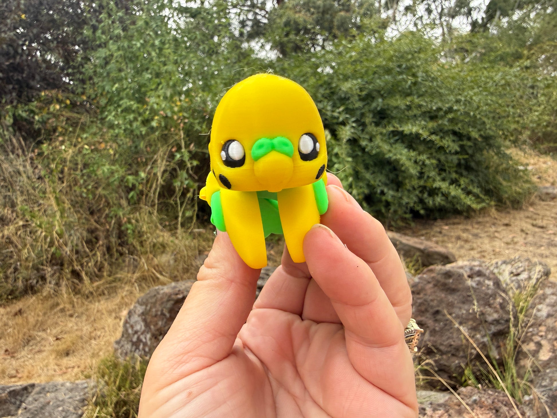 Yellow and green t3d printed budgie figure held in a hand with a natural background