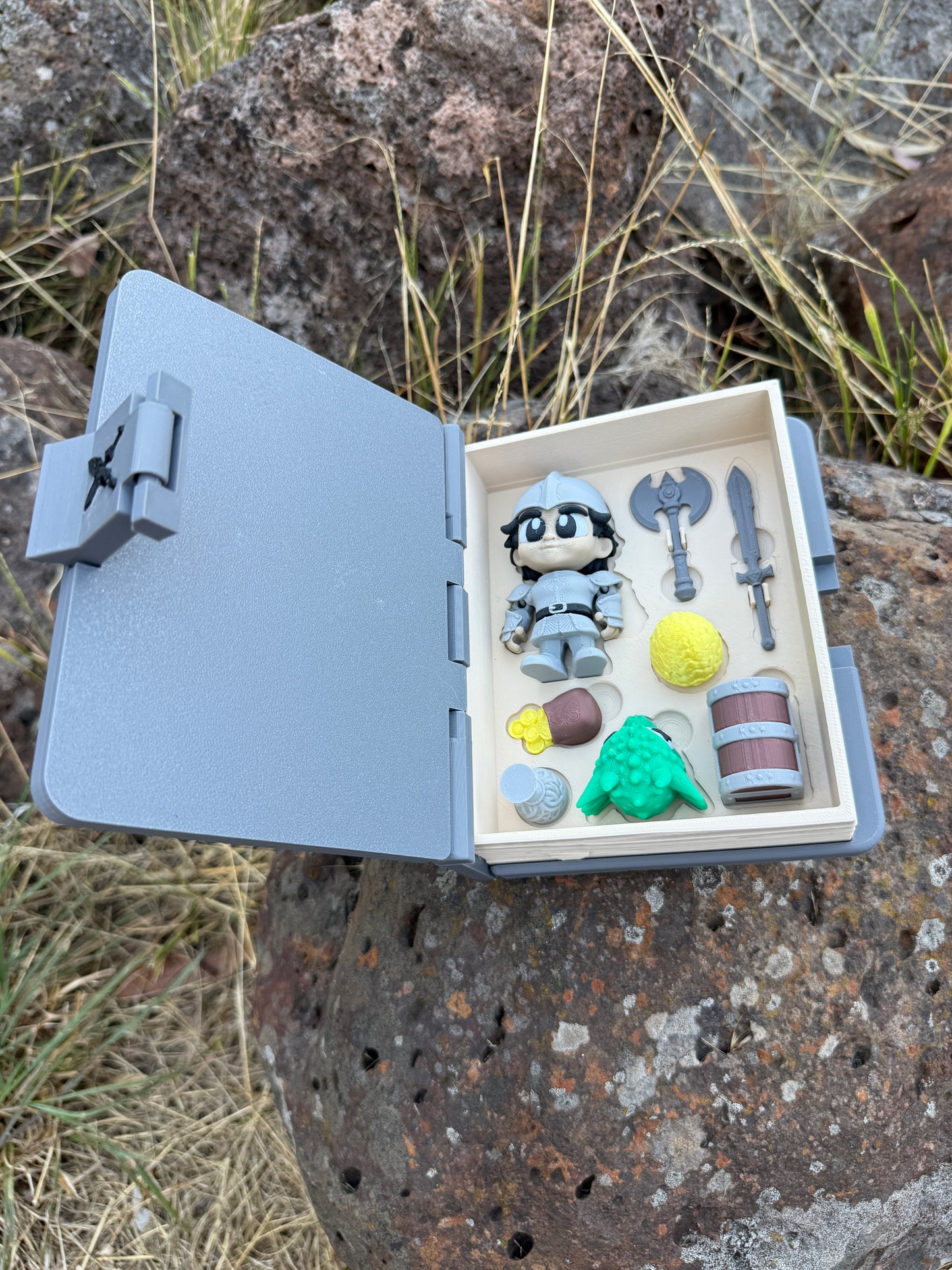 Small open 3d printed book with miniature items on a rocky surface