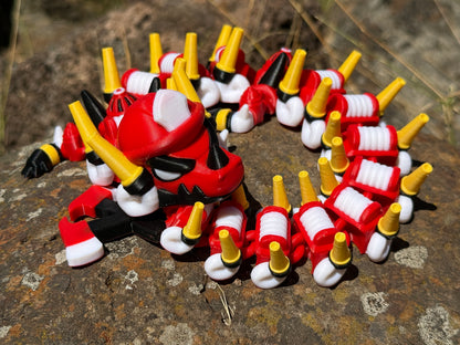 firefighter dragon 3d printer with red, white, and yellow segments on a rocky surface with a 2-axe tail