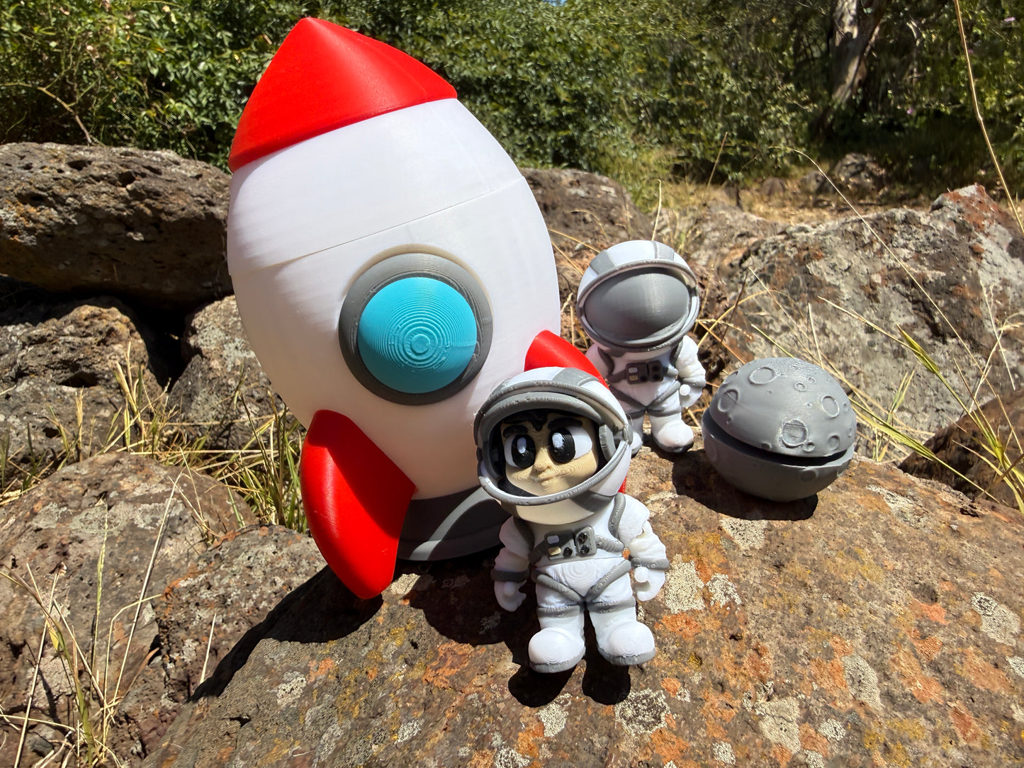 Toy rocket and astronaut figure on a rocky surface with greenery in the background