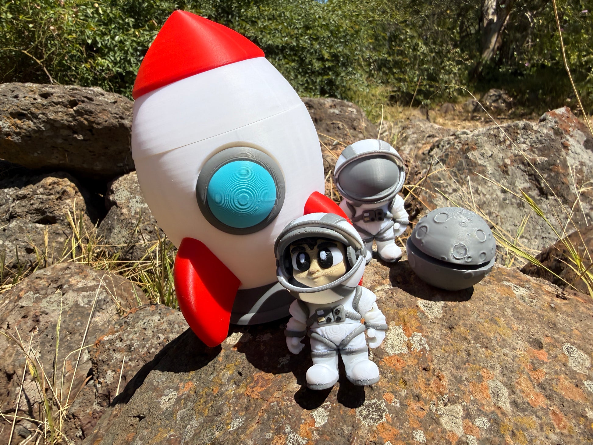 Toy rocket and astronaut figure on a rocky surface with greenery in the background