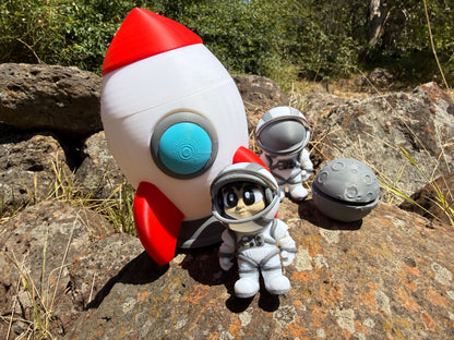 Toy rocket and astronaut figure on a rocky surface with greenery in the background