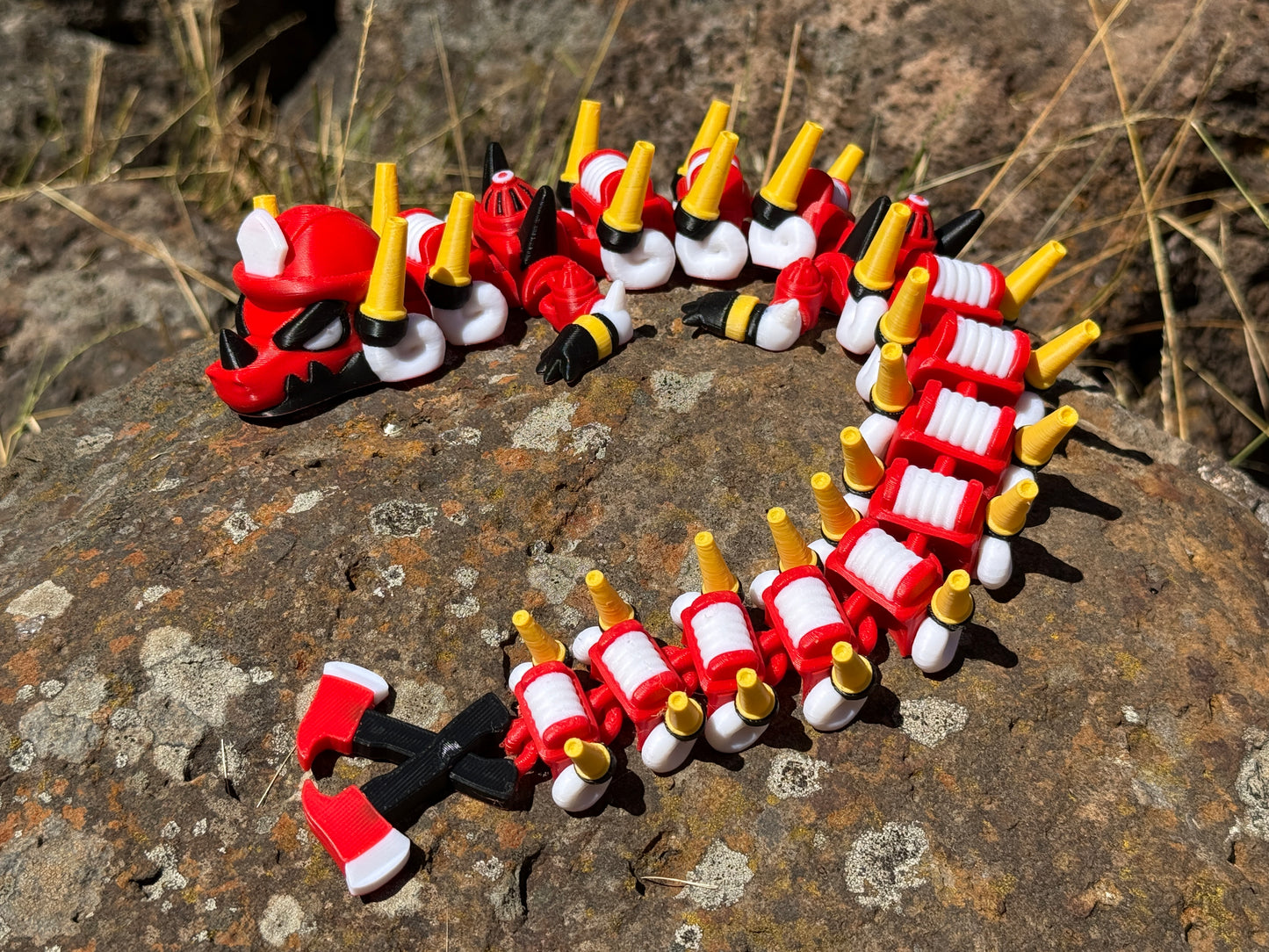 firefighter dragon 3d printer with red, white, and yellow segments on a rocky surface with a 2-axe tail