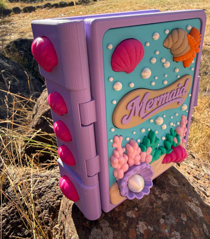 Colour purple, blue, white, green, pink 3d printed book with mermaid design on a rock