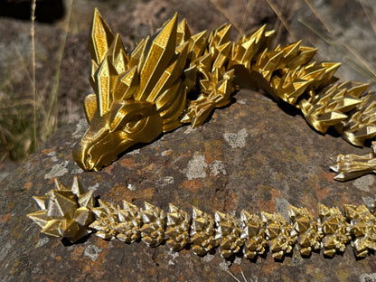 Gold silver 3d printed 
dragon sculpture on a textured stone surface