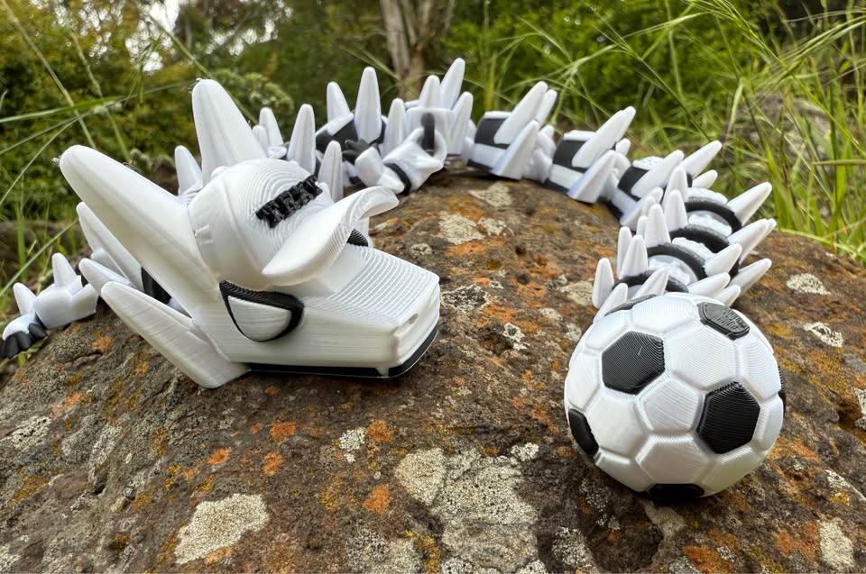 3d printed dragon white and black. with a soccer ball tail and a white hat with text 