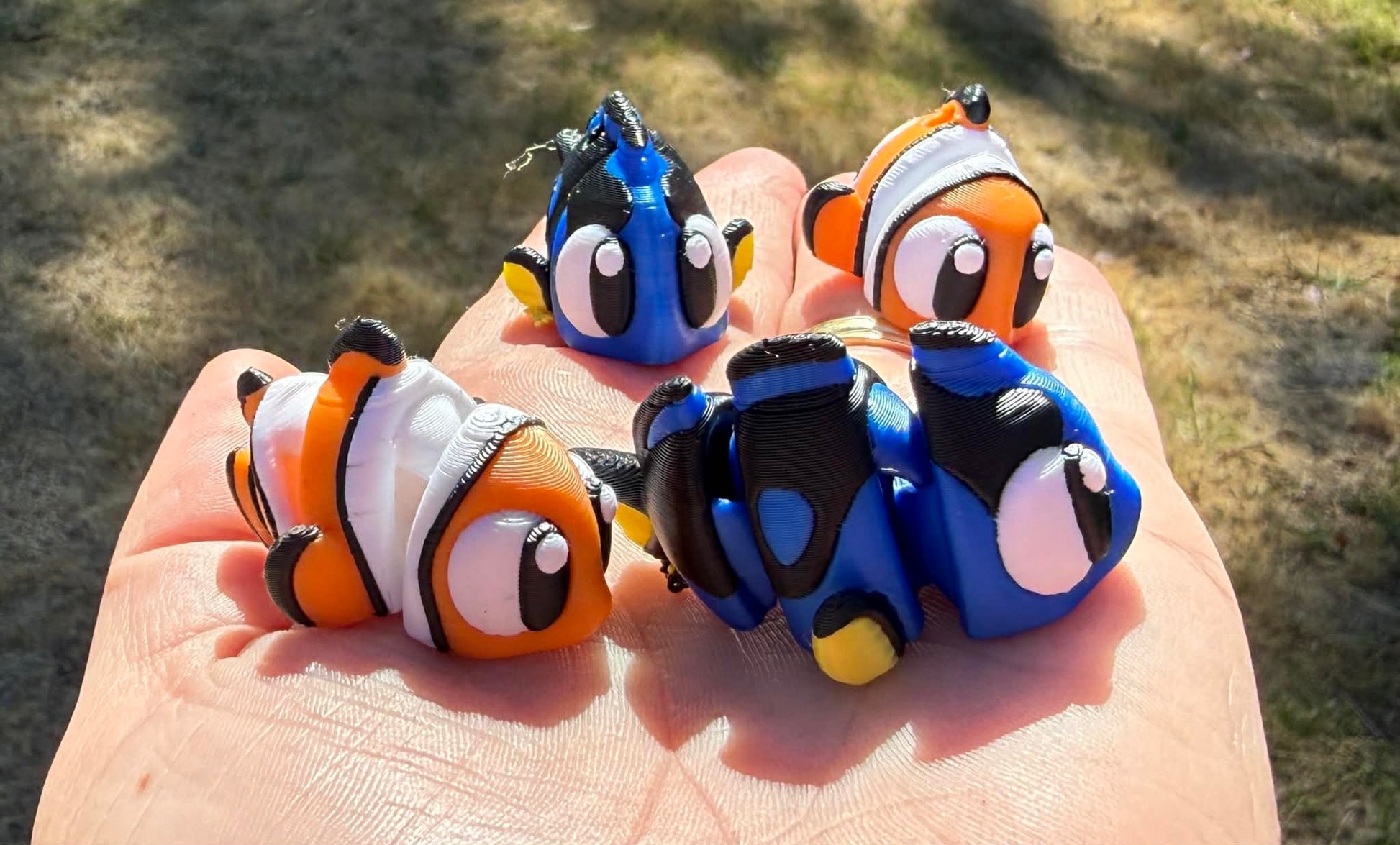 Four small fish-shaped 3d printed held in a hand with a blurred natural background