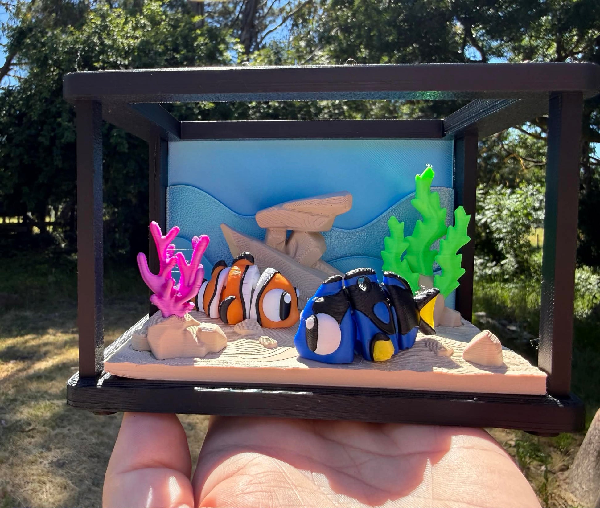 Model of clown fish and blue tang from 'Finding Nemo' in a tank with coral and rocks.