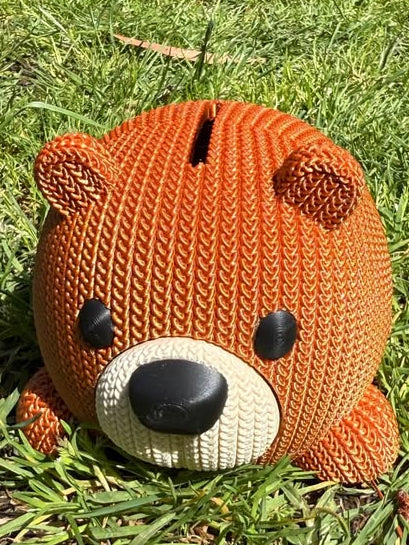 Knitted look money box bear shape with a face on grass