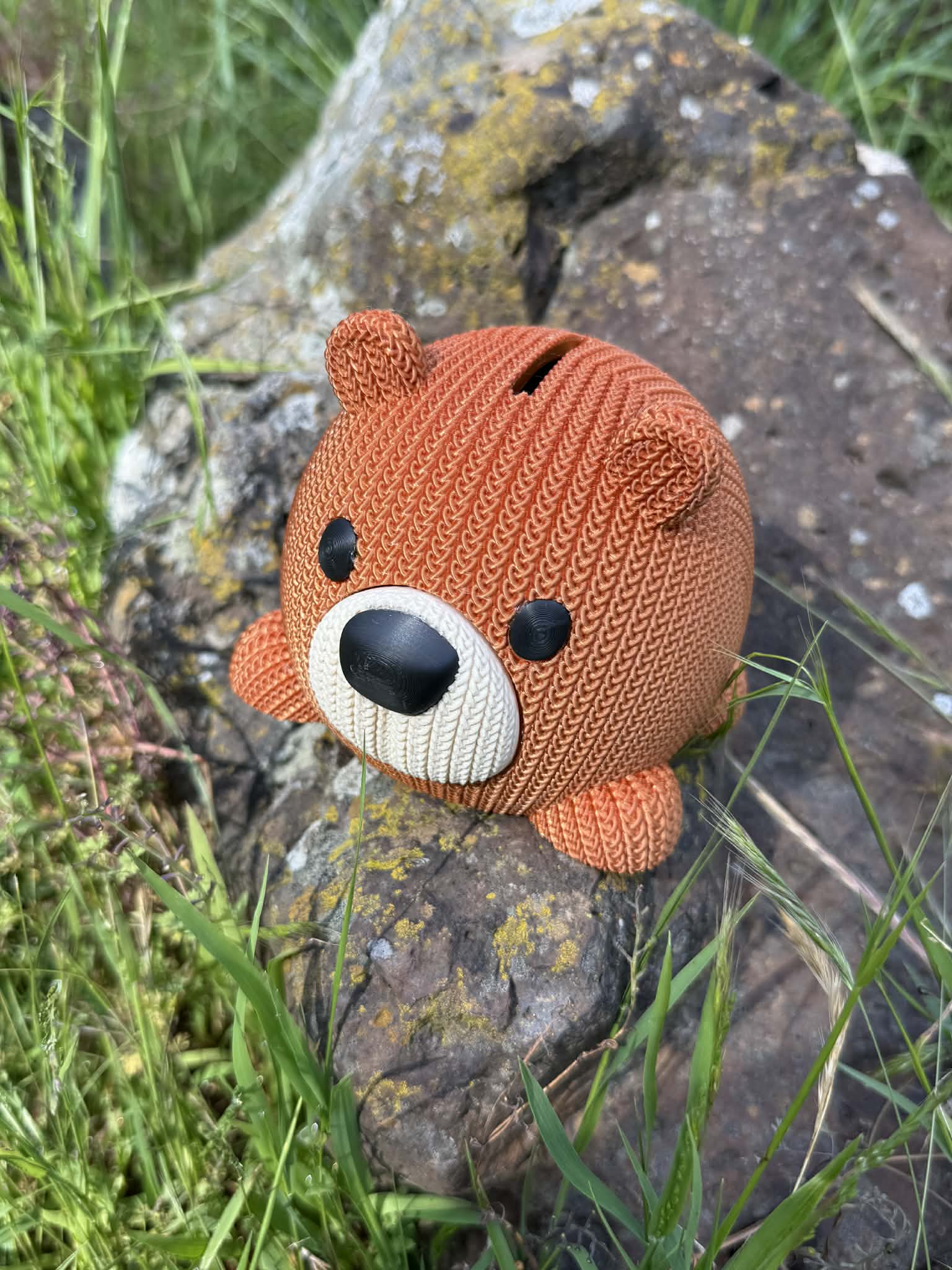 Knitted bear-shaped money box on a stone surface with grass in the background