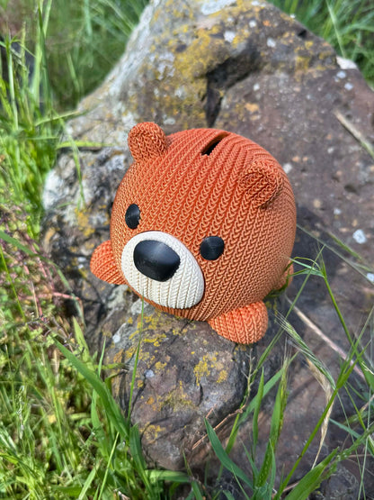 Knitted bear-shaped money box on a stone surface with grass in the background