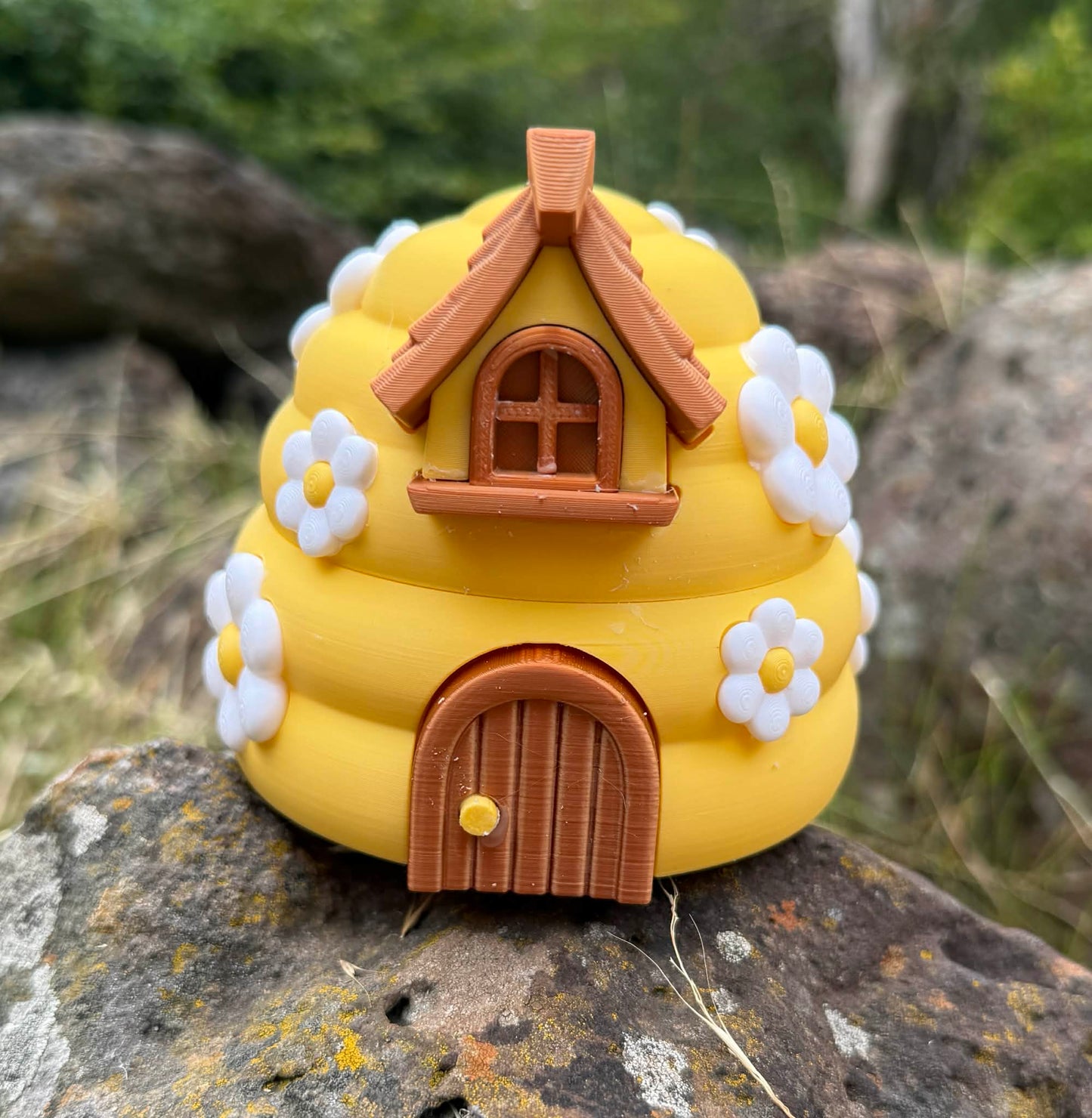 Yellow 3D printed beehive with brown roof and door on a rock