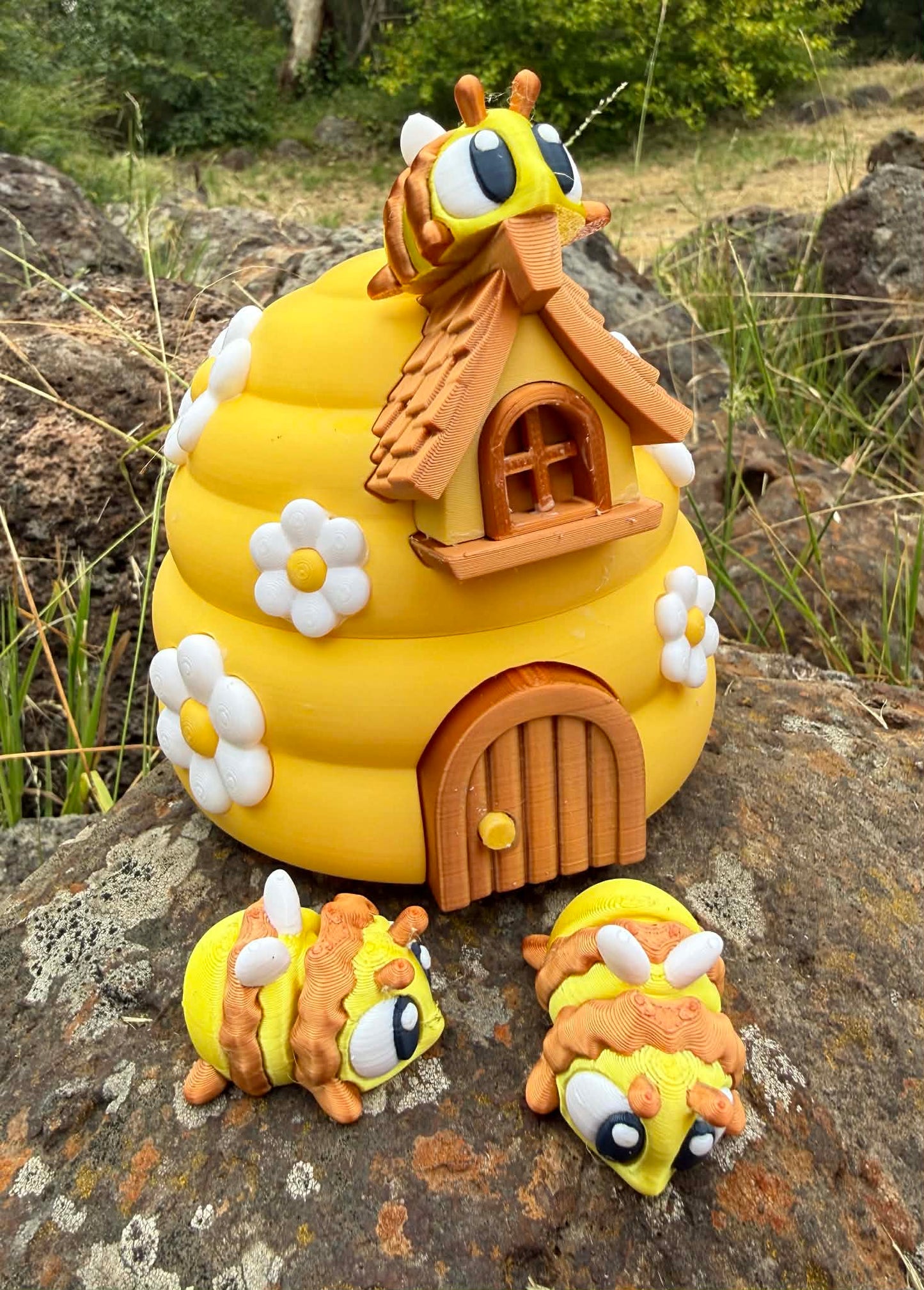 Yellow 3D printed beehive with three 3D printed bee characters on a rock