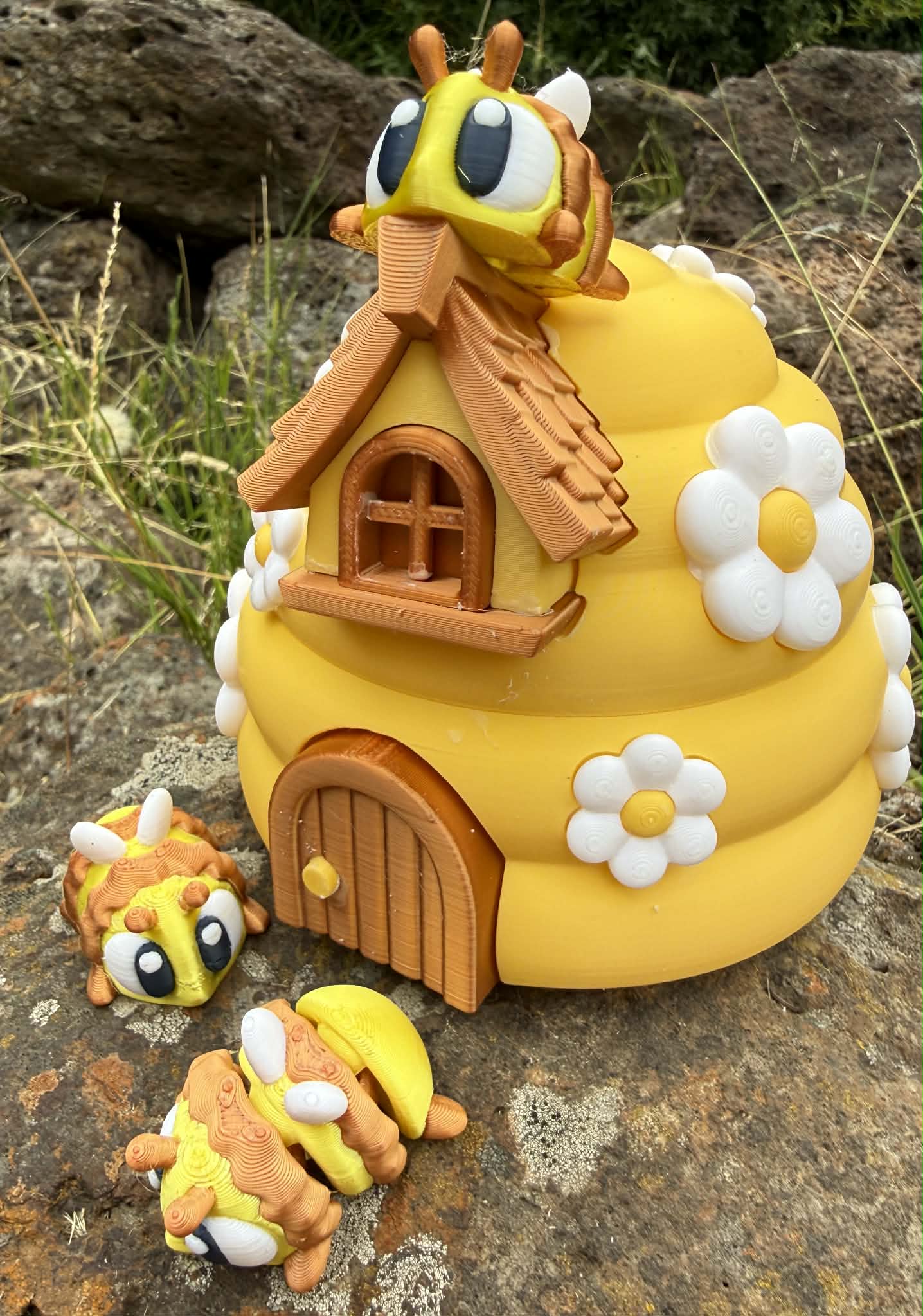 Yellow 3D printed bee-shaped house with 3D printed bee characters on a stone surface