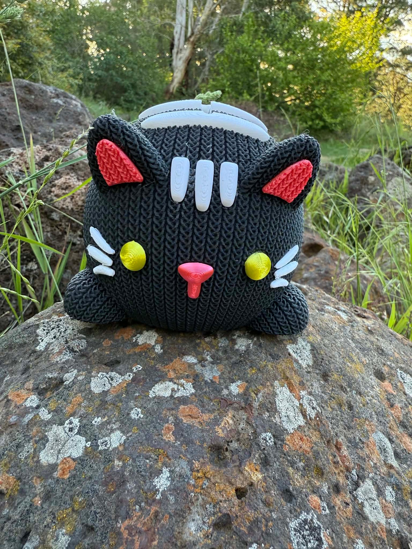 Black knitted cat 3D printed with colorful accents on a rock outdoors