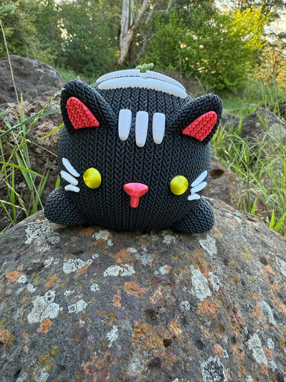 Black knitted cat 3D printed with colorful accents on a rock outdoors