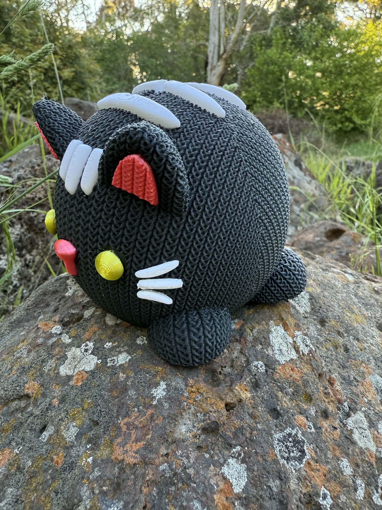 Knitted cat 3d printed money box black and white on a rock with a natural background