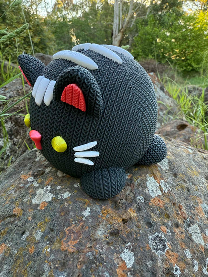 Knitted cat 3d printed money box black and white on a rock with a natural background