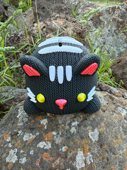 Black and white with yellow eyes and pink nose Knitted cat money box 3d printed on a rock with grass in the background