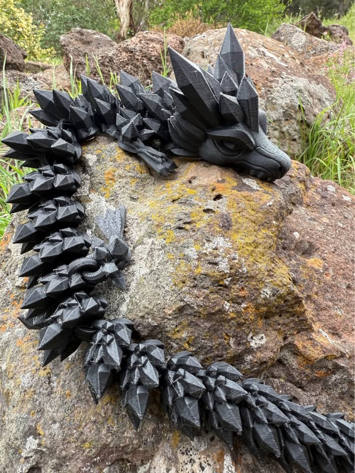 Black dragon 3d printed on a rock with grass and trees in the background