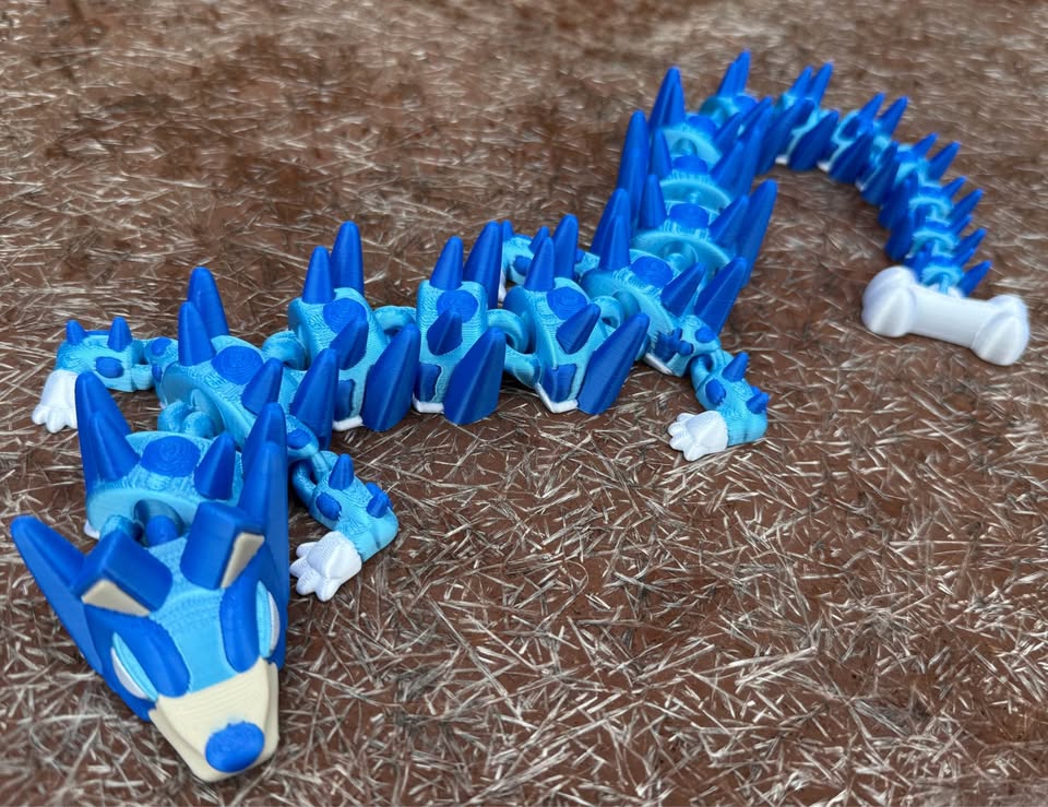 Blue 3d printed dog dragon with a small bone on the end of its tail 
on a brown textured surface