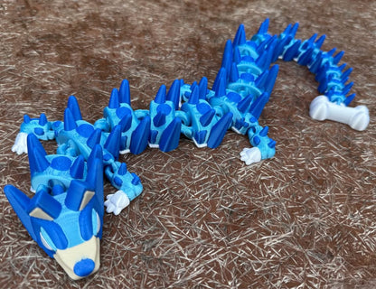 Blue 3d printed dog dragon with a small bone on the end of its tail 
on a brown textured surface