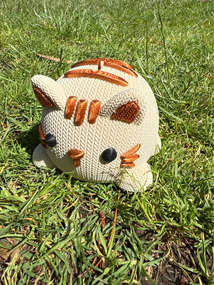 Beige and copper Knitted cat-shaped 3D printed money box on grass
