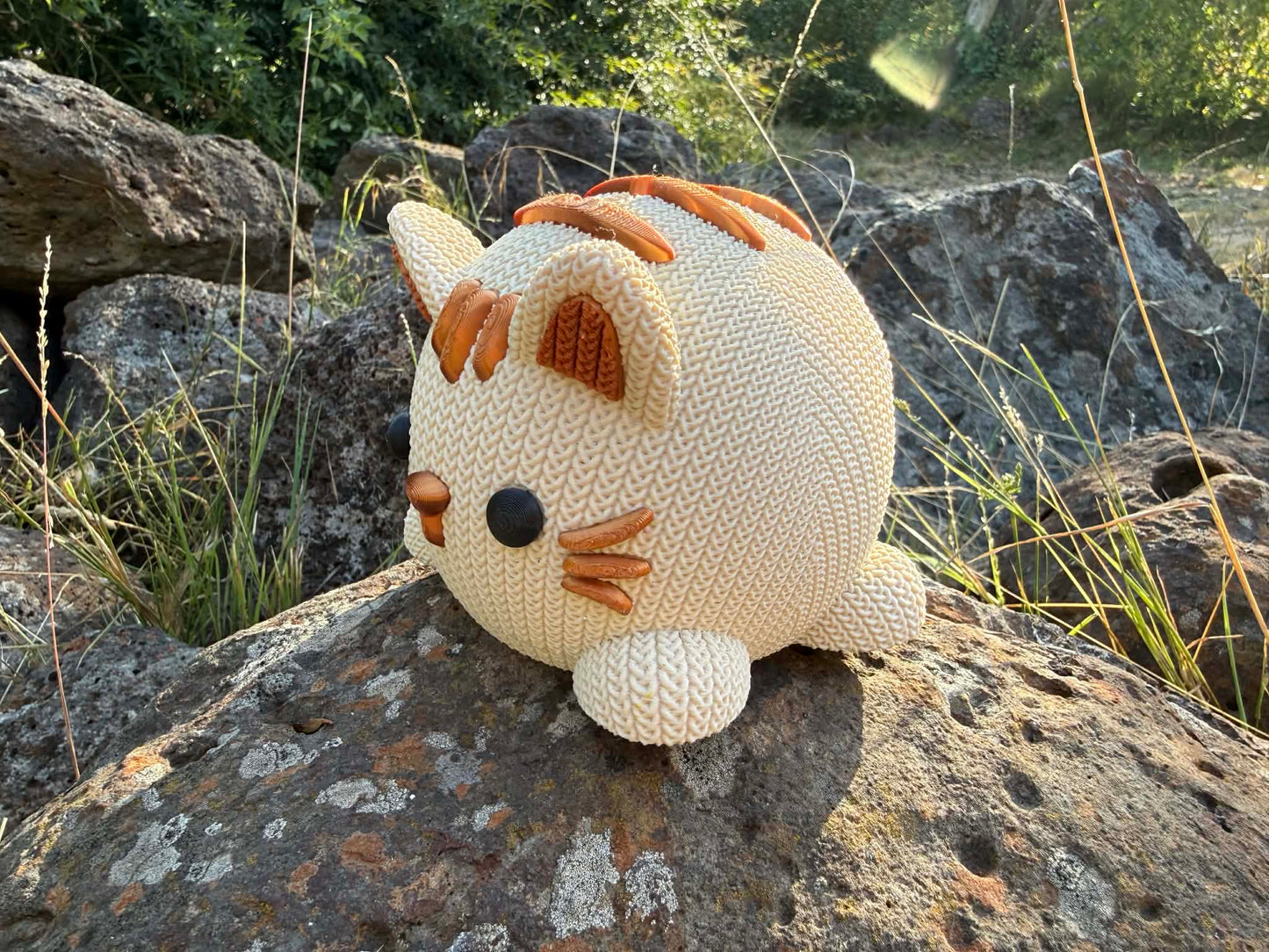 Knitted cat 3d printed beige and copper colour on a rock with natural background