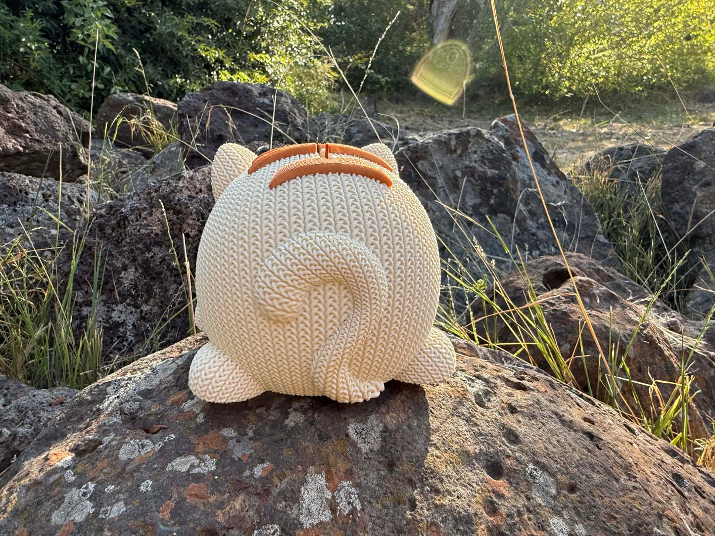 Knitted back of cat money box showing tail. beige and copper colour  on a rock with natural background