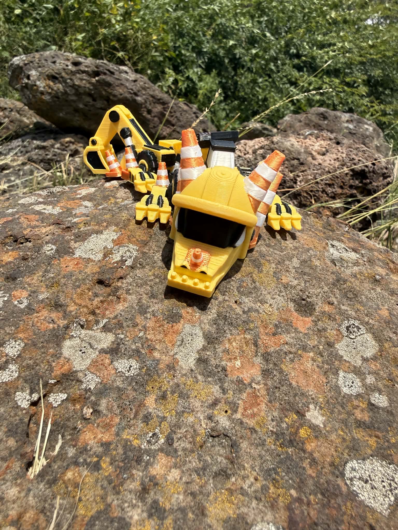 3D printed excavator mini dragon with traffic cones on a rocky surface. front view