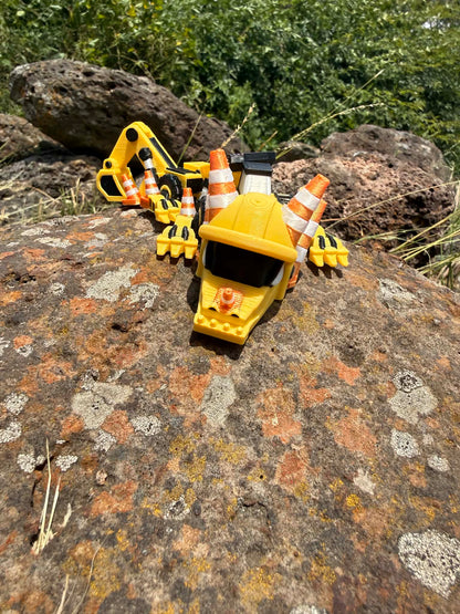 3D printed excavator mini dragon with traffic cones on a rocky surface. front view