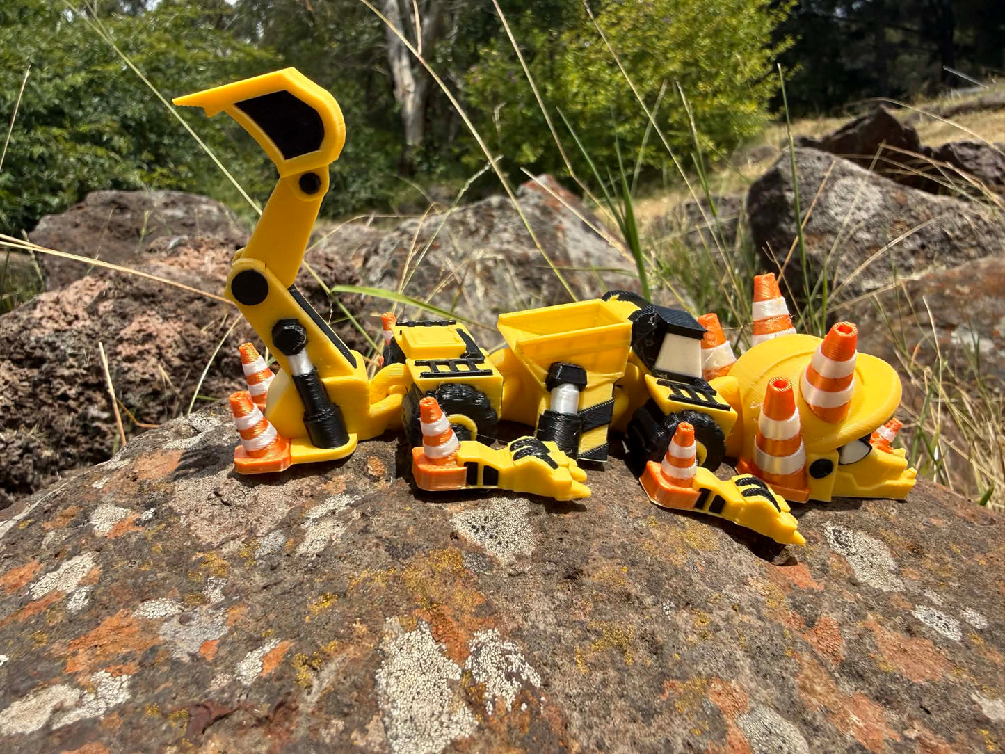 3D printed excavator mini dragon with traffic cones on a rocky surface. tail up showing usable bucket