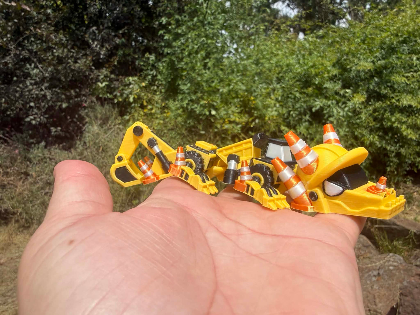 3D printed excavator mini dragon with traffic cones on the palm of a hand