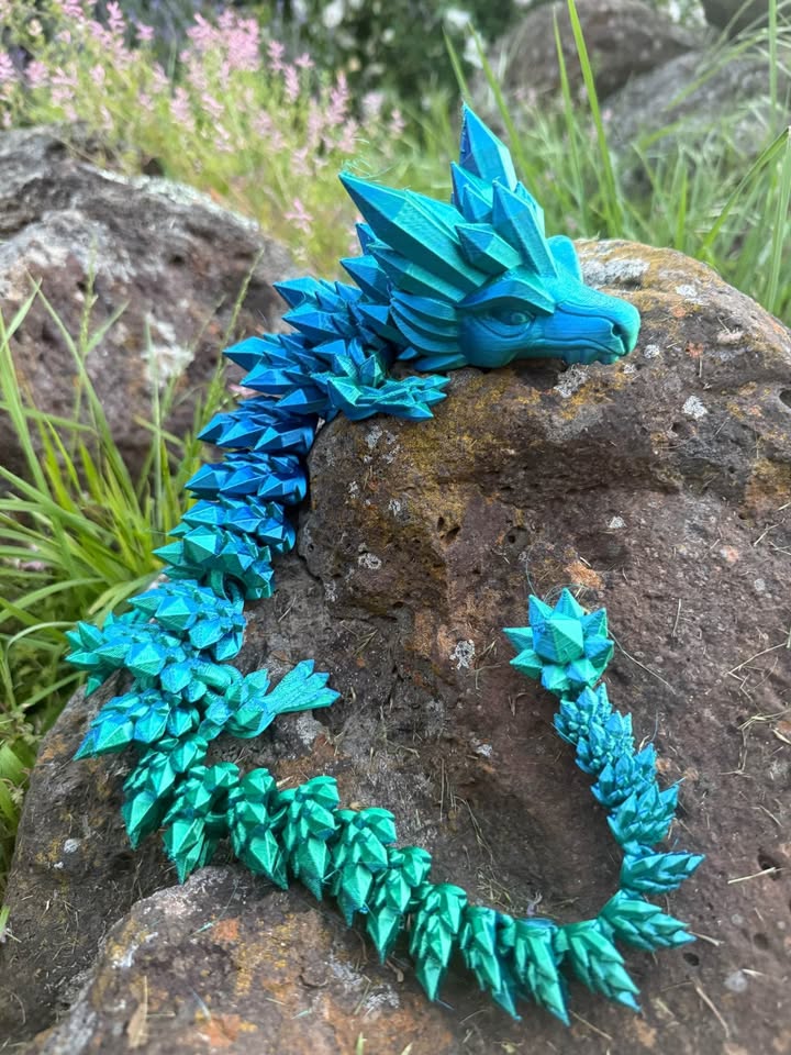 Turquoise dragon 3d print on a rock with grass in the background