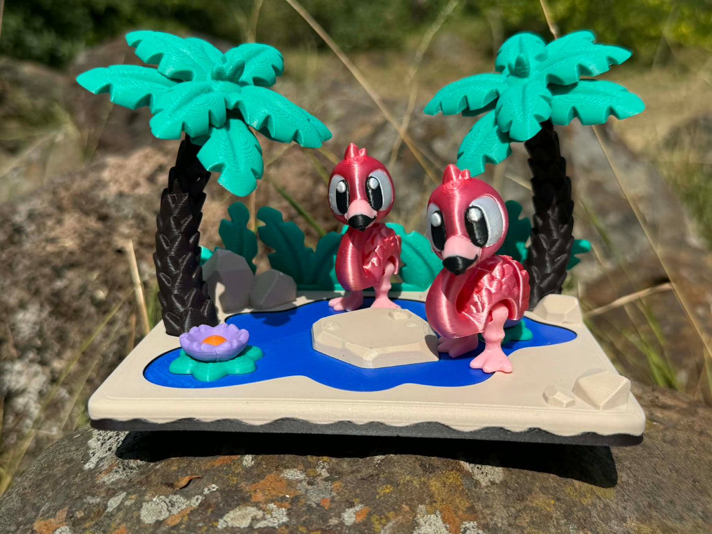 Two pink flamingoes 3d printed articulated characters on a miniature landscape with palm trees and a pond.