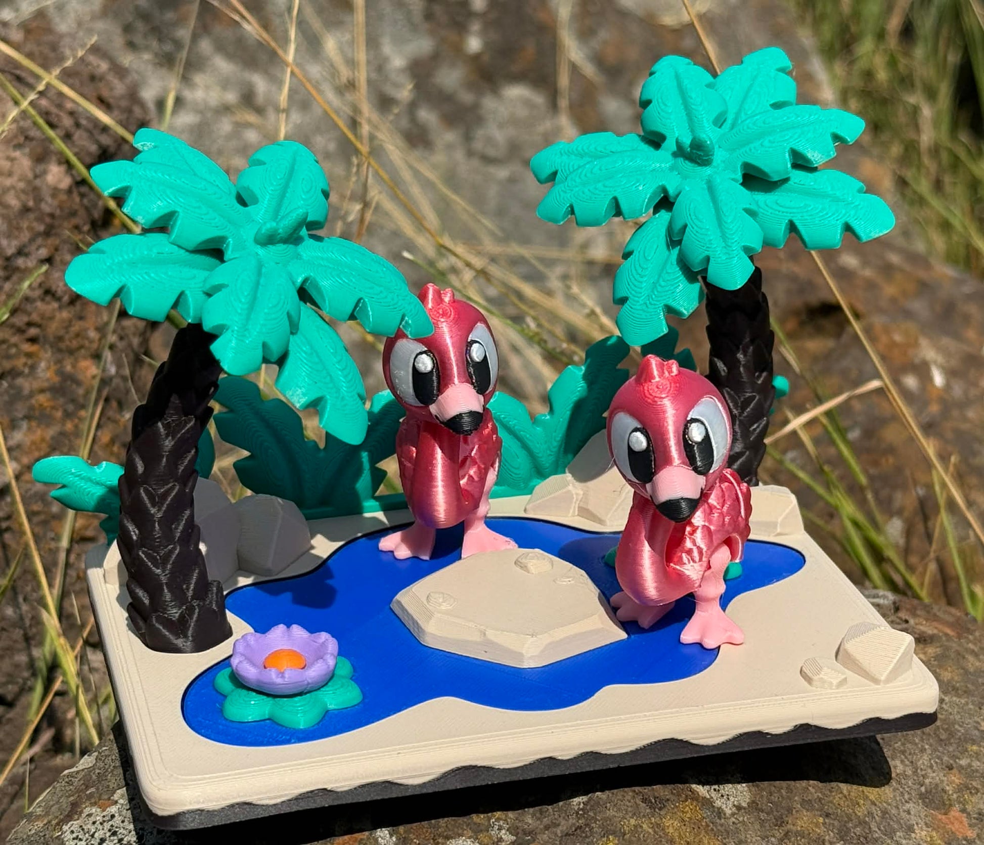 Two pink flamingoes 3d printed articulated characters on a miniature landscape with palm trees and a pond.