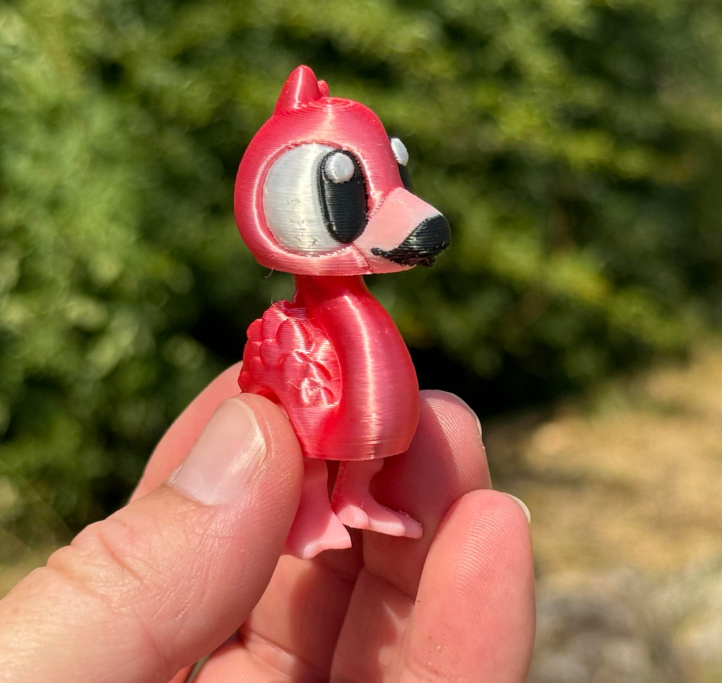 Small pink flamingo 3d printed figurine held in a hand with a blurred green outdoor background