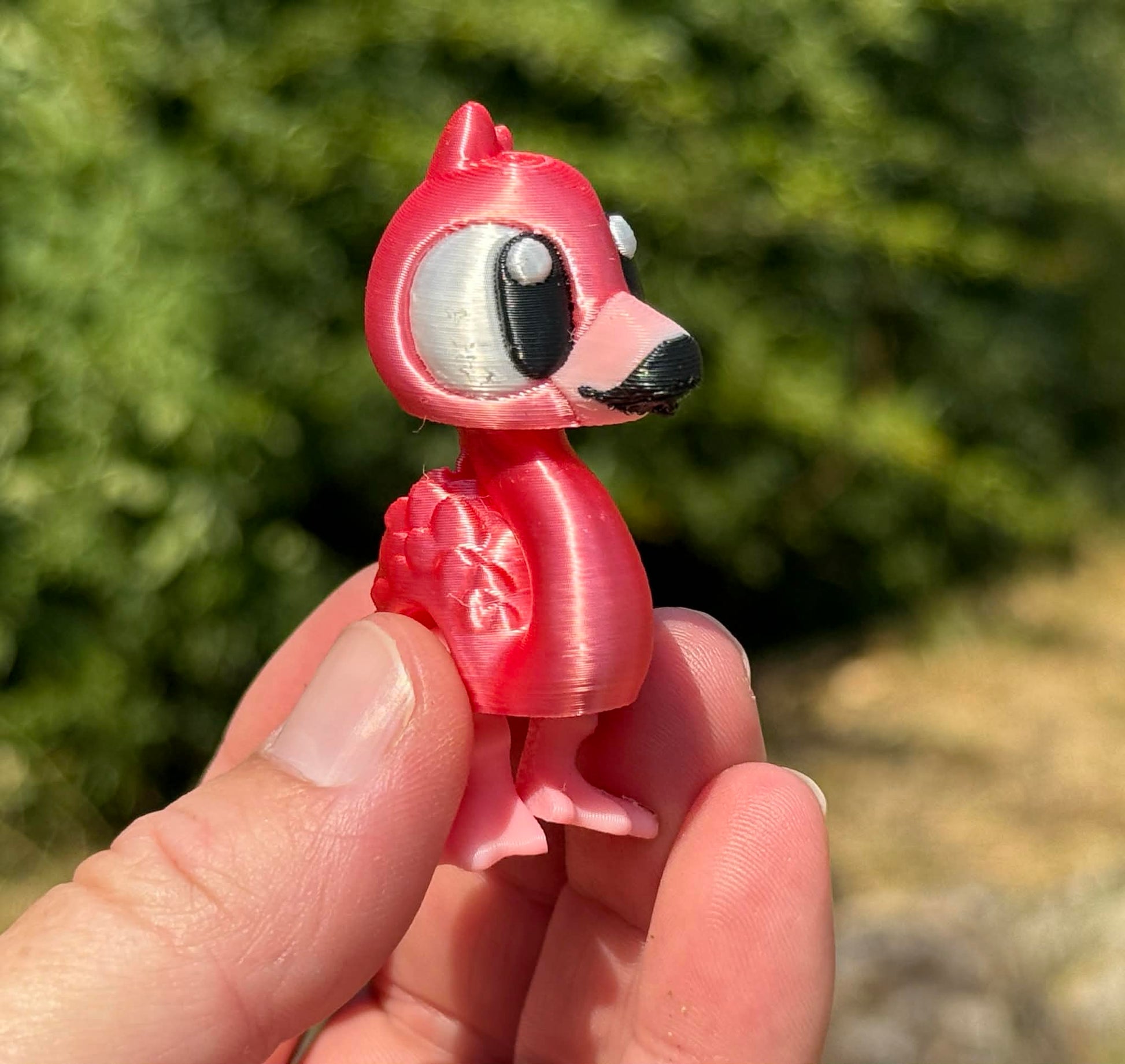 Small pink flamingo 3d printed figurine held in a hand with a blurred green outdoor background